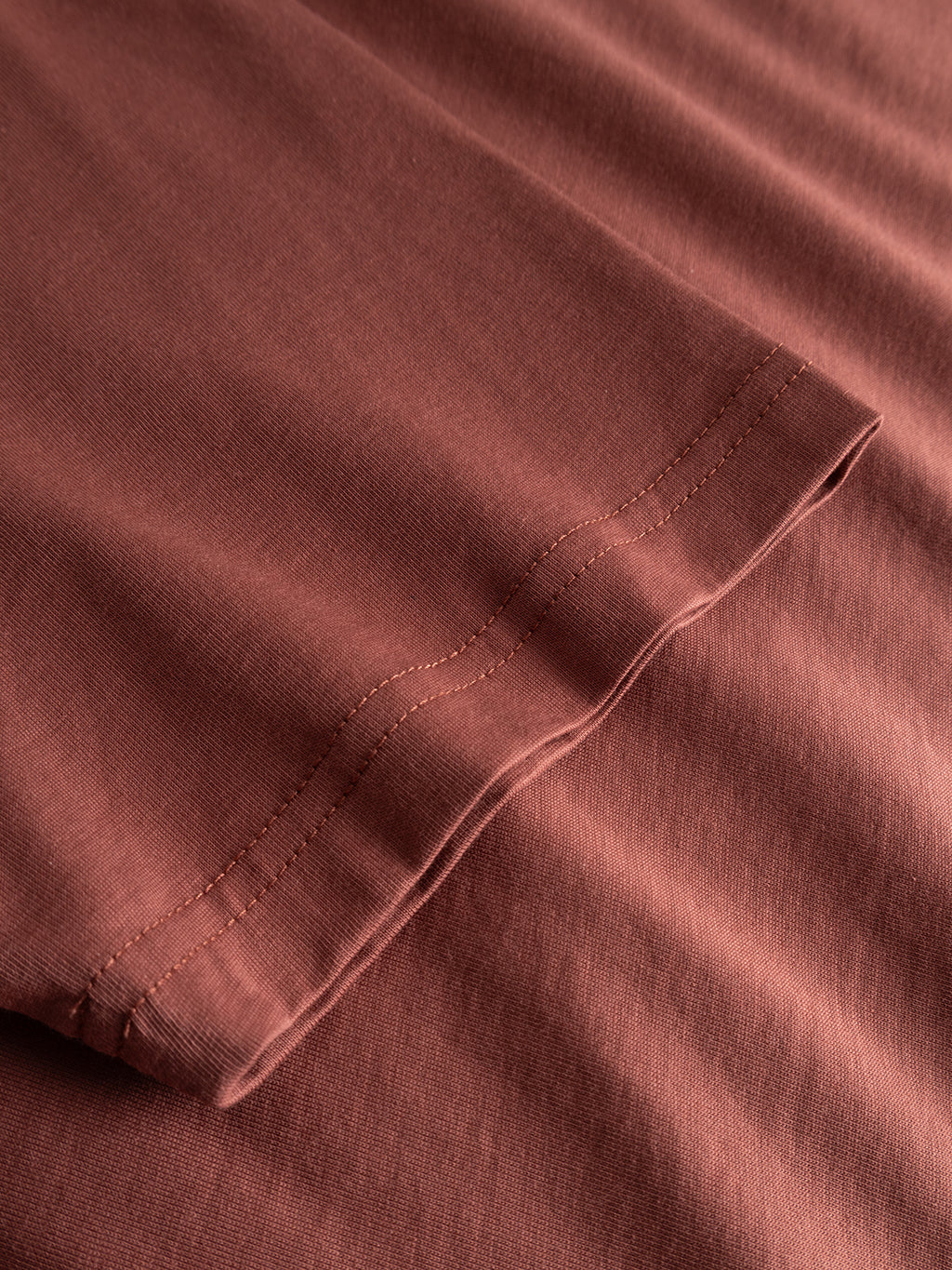 Close-up of the hem and sleeve of the Gabba GABdune Logo GOTS SS T-Shirt in Brick Red, highlighting the stitching details and texture of its organic cotton fabric.