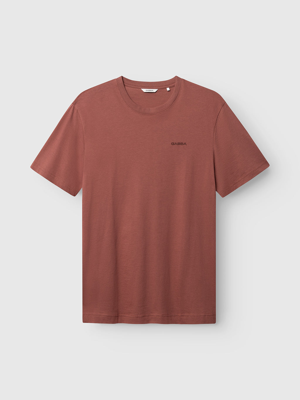 The GABdune Logo GOTS SS T-Shirt by Gabba in Brick Red features a classic fit with short sleeves, a round neckline, and a small black text logo on the left chest. The shirt is shown against a light gray background.
