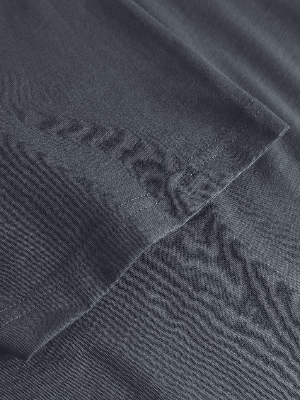 Close-up of the Gabba GABdune Logo GOTS SS T-Shirt in Turbulence Blue, highlighting the organic cotton fabric’s texture and double stitching detail along the hem against a matching background.