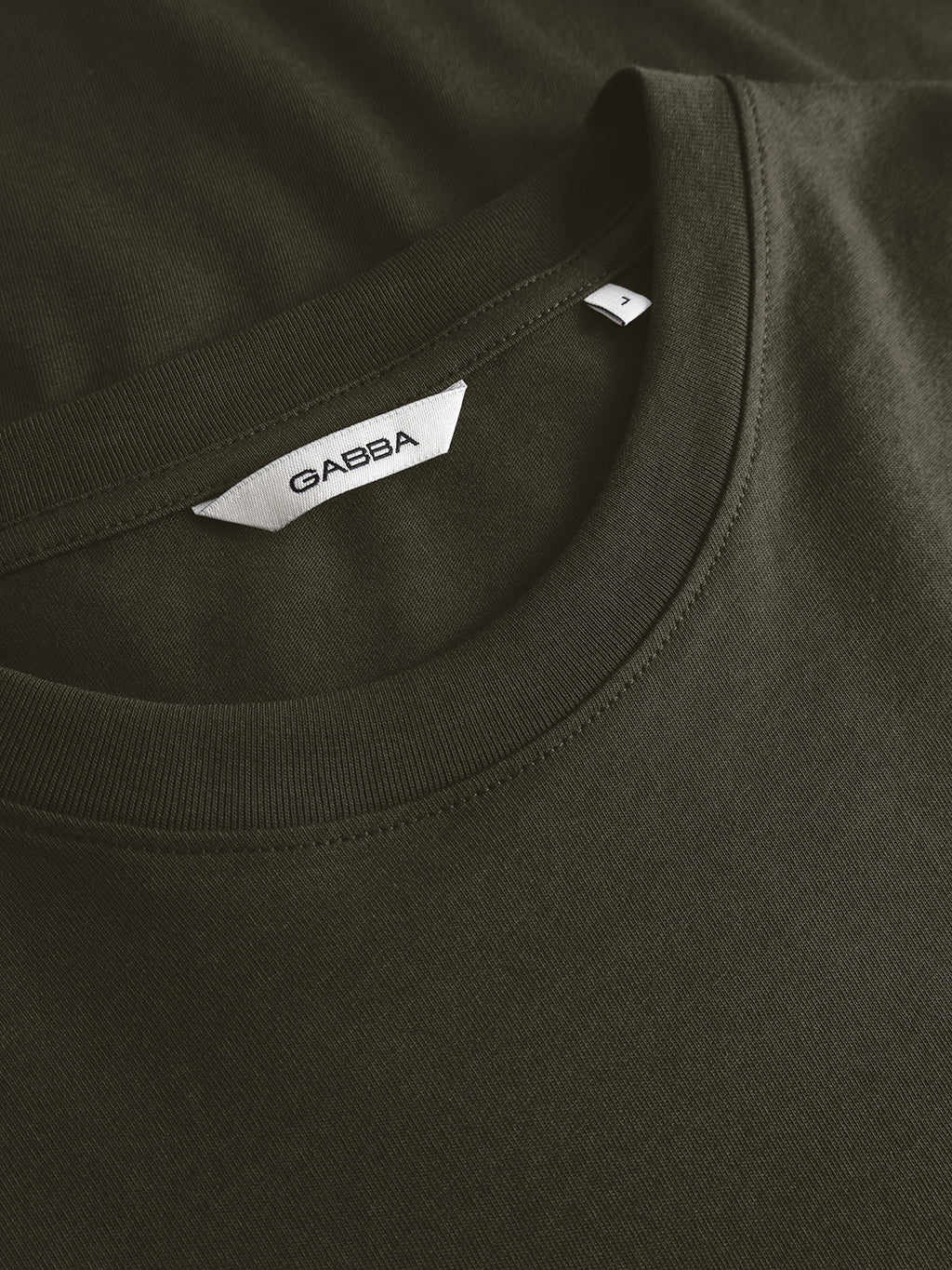 Close-up of the GABdune Logo GOTS SS T-Shirt in Forest Night by Gabba, a dark green, classic-fit tee featuring a white label with the brand name at the collar and part of the upper chest area visible.