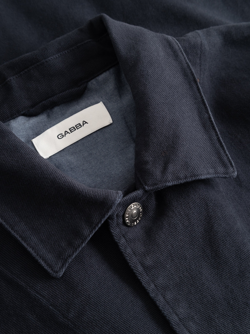Close-up of the GABbeta Twill - Navy shirt by Gabba, featuring a dark blue collar with a button and a visible white label inside reading “Gabba.” Made from garment-dyed stretch twill, the fabric displays a subtle diagonal texture that enhances both depth and comfort.
