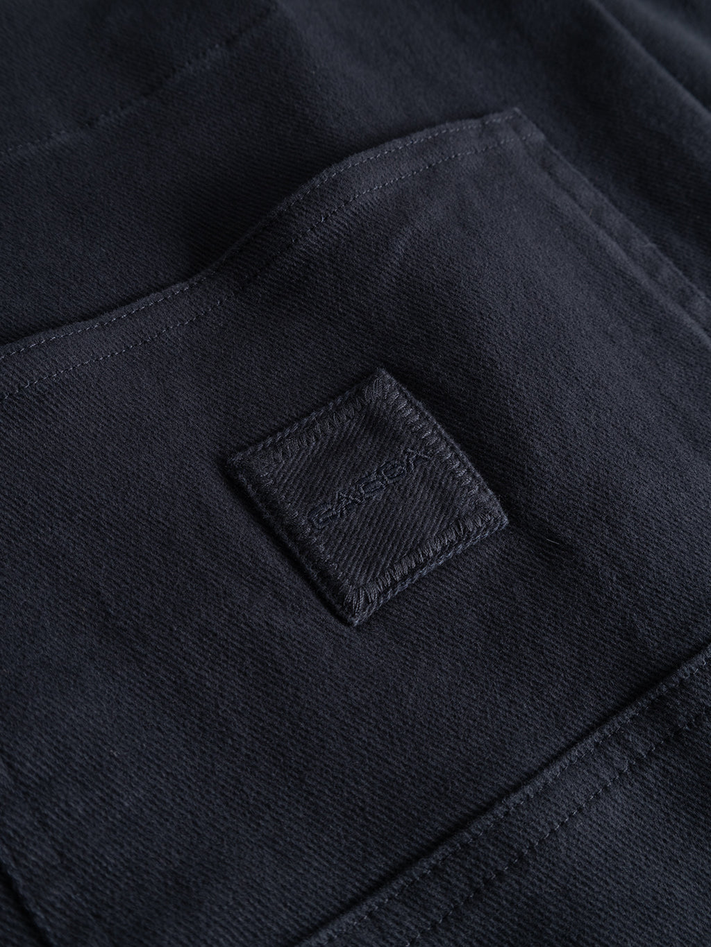 A close-up of the Gabba GABbeta Twill - Navy shows a dark garment-dyed stretch twill fabric pocket, featuring a small stitched square label with subtle text. The detailed stitching and distinct fabric texture highlight the quality craftsmanship typical of utility pockets.