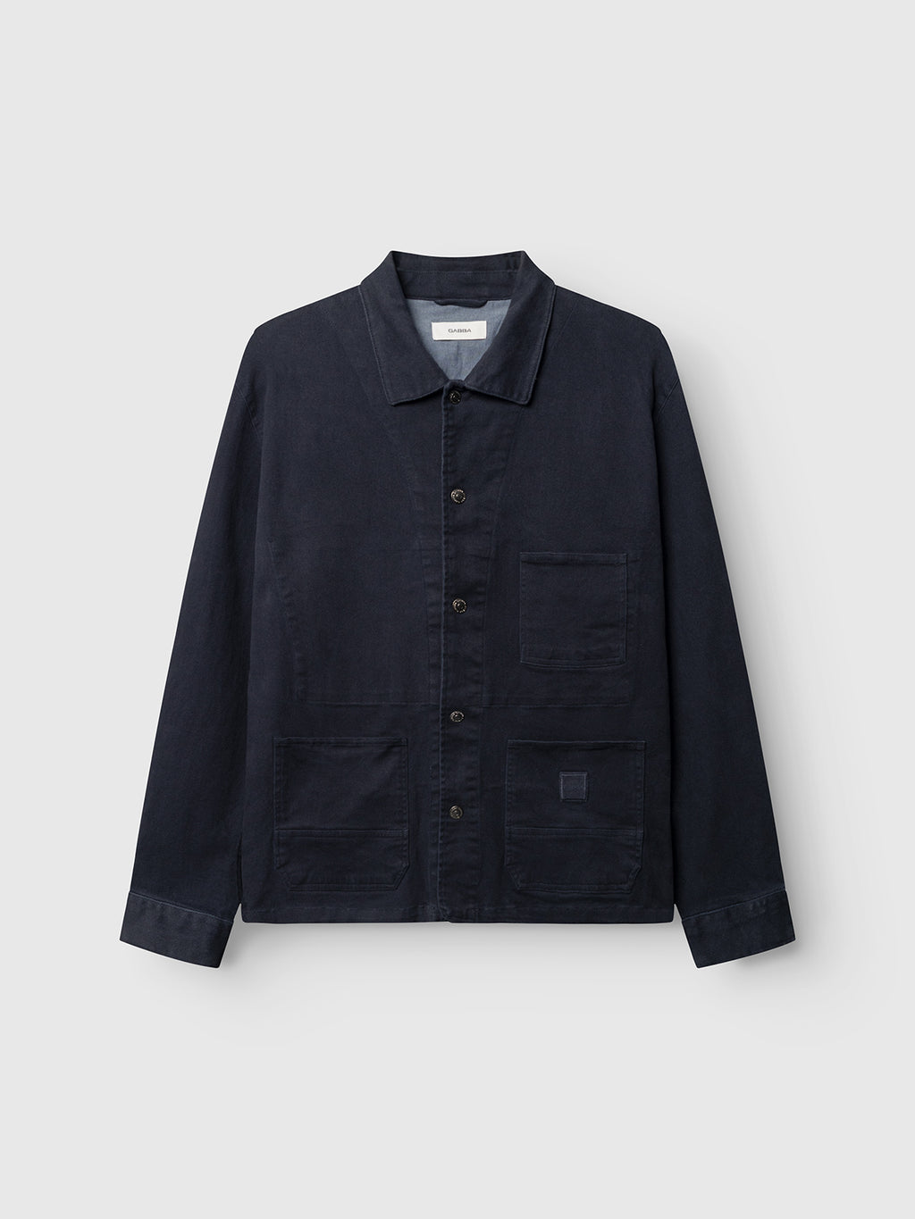 The GABbeta Twill - Navy chore jacket by Gabba features a collar, button-up front, and three utility pockets, crafted from garment-dyed stretch twill for comfort and durability, and is displayed on a plain light gray background.