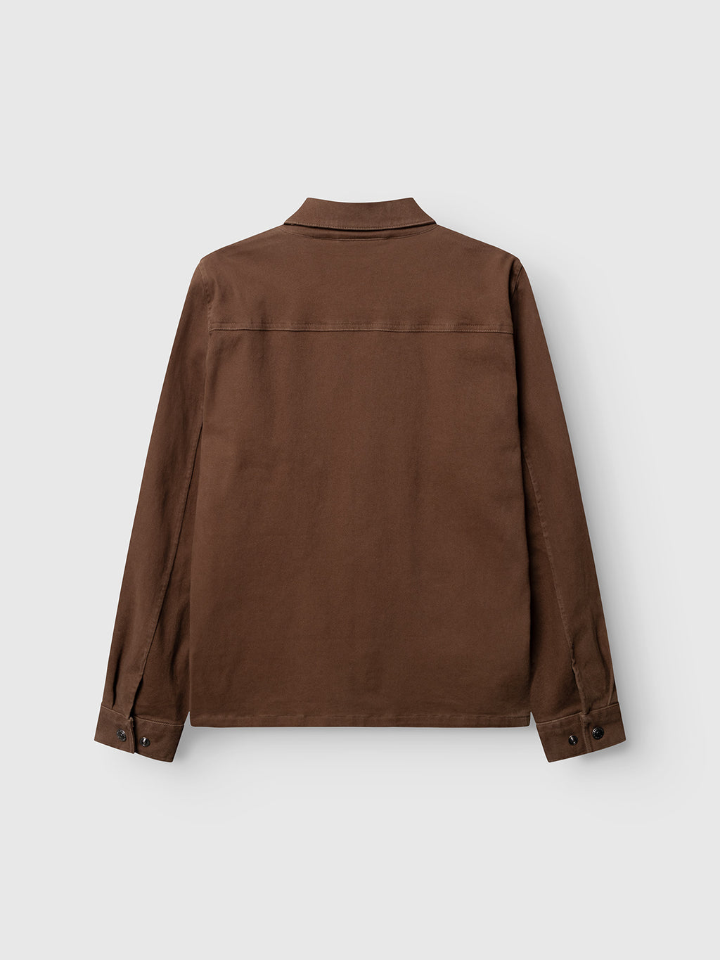 The Gabba GABbeta Twill - Brown Slate jacket is displayed from the back, highlighting its long sleeves, collared neckline, buttoned cuffs, and minimalist design against a light gray background. Made from garment-dyed stretch twill, this piece seamlessly combines subtle comfort with a workwear-inspired silhouette.