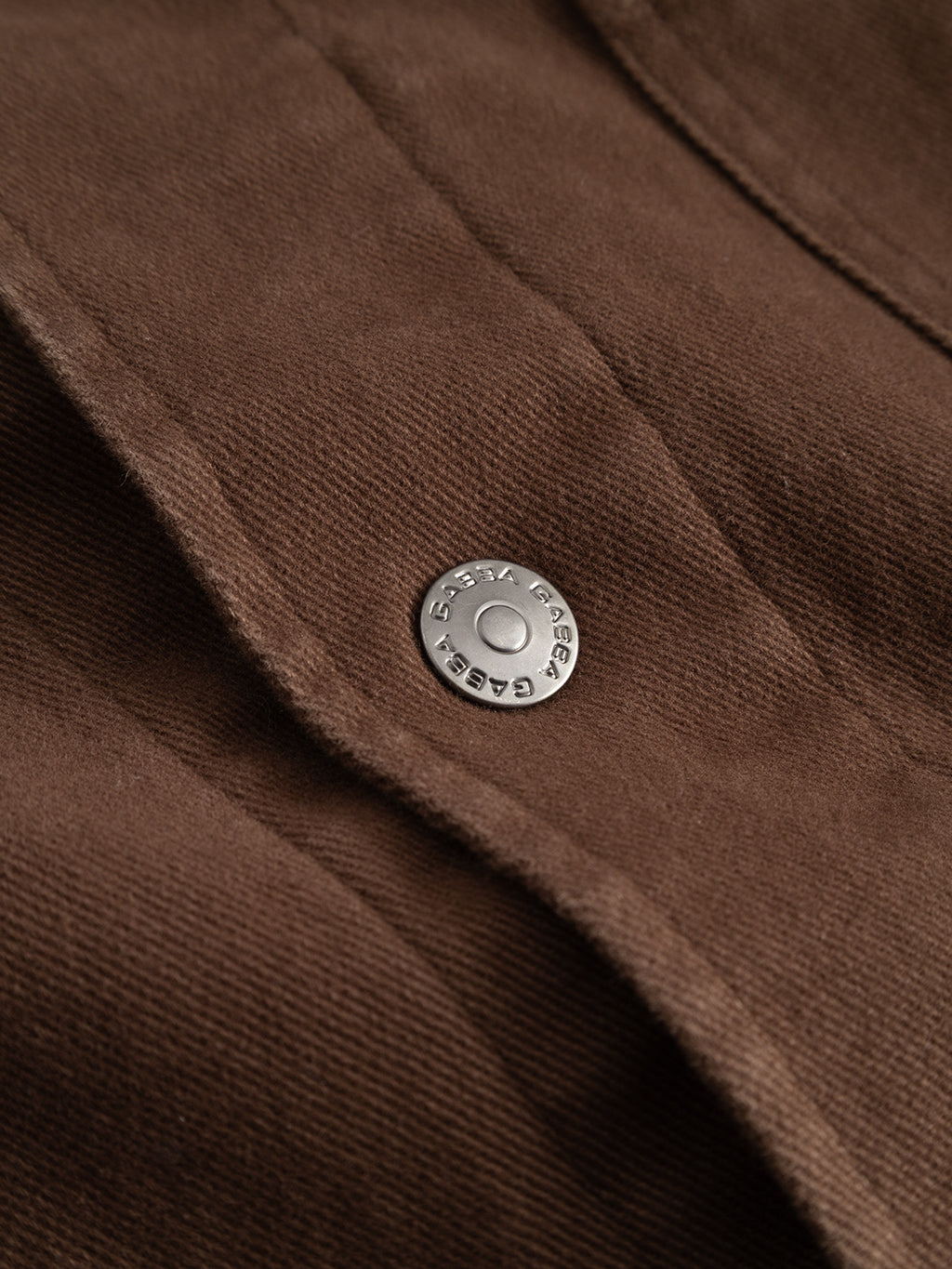 Close-up of the Gabba GABbeta Twill - Brown Slate, showcasing its garment-dyed stretch twill fabric with a metallic snap button engraved with “5 SETTA GARAGE 8927.” The visible fabric texture and stitching highlight the workwear-inspired silhouette.