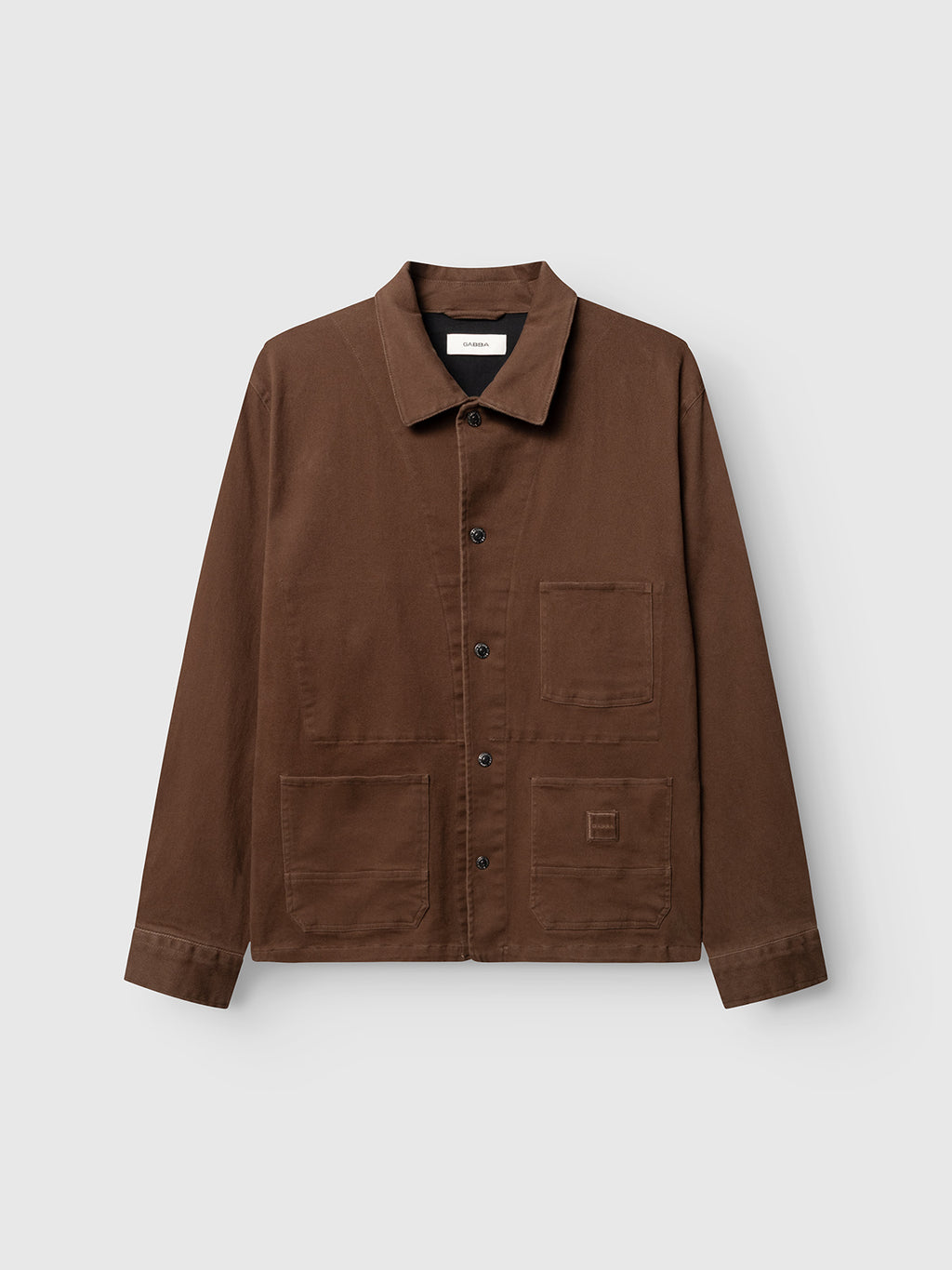 The Gabba GABbeta Twill - Brown Slate is a button-up chore jacket made from garment-dyed stretch twill, featuring a collar and three front utility pockets in a workwear-inspired silhouette, showcased against a plain light gray background.