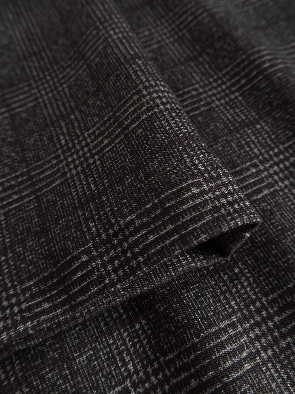 A close-up of Gabba’s GABpaul Nygo - Grey Check fabric reveals a detailed grey check pattern with intersecting lines, featuring a folded edge and textured finish—crafted from comfort stretch material for everyday wear.