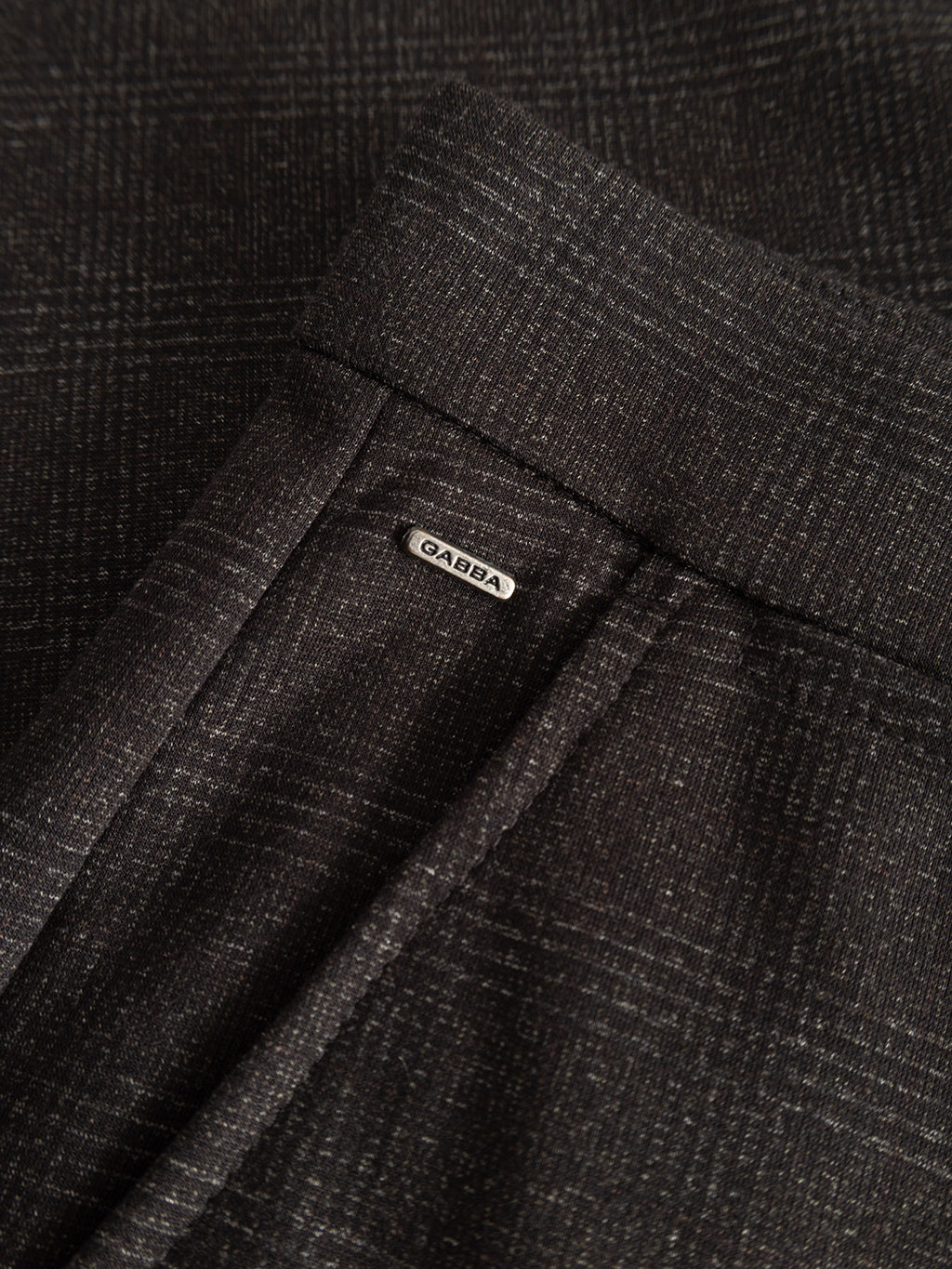 Close-up of the Gabba GABpaul Nygo - Brown Check, showcasing its dark plaid-patterned fabric and a small metallic Gabba label near the seam—highlighting a stylish, textured garment made from comfort stretch fabric, perfect for everyday wear.