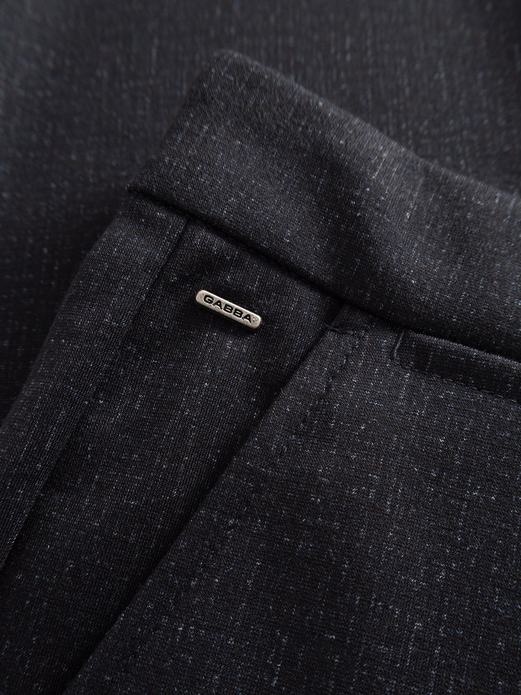 Close-up of GABpaul Nygo - Night Sky pants by Gabba, showcasing dark fabric with a textured pattern and a small metallic GABBA tag near the front pocket—crafted in a versatile chino style from comfort stretch material for effortless everyday wear.