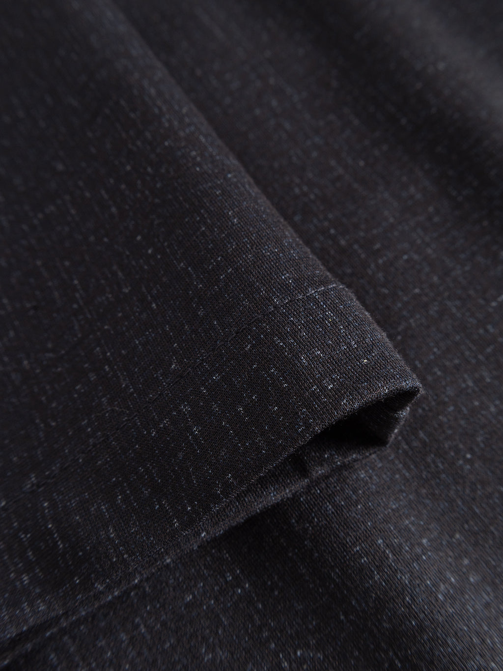 Close-up of folded GABpaul Nygo - Night Sky comfort stretch fabric by Gabba, featuring a dark hue with a subtle heather pattern, fine white specks, and a smooth texture.