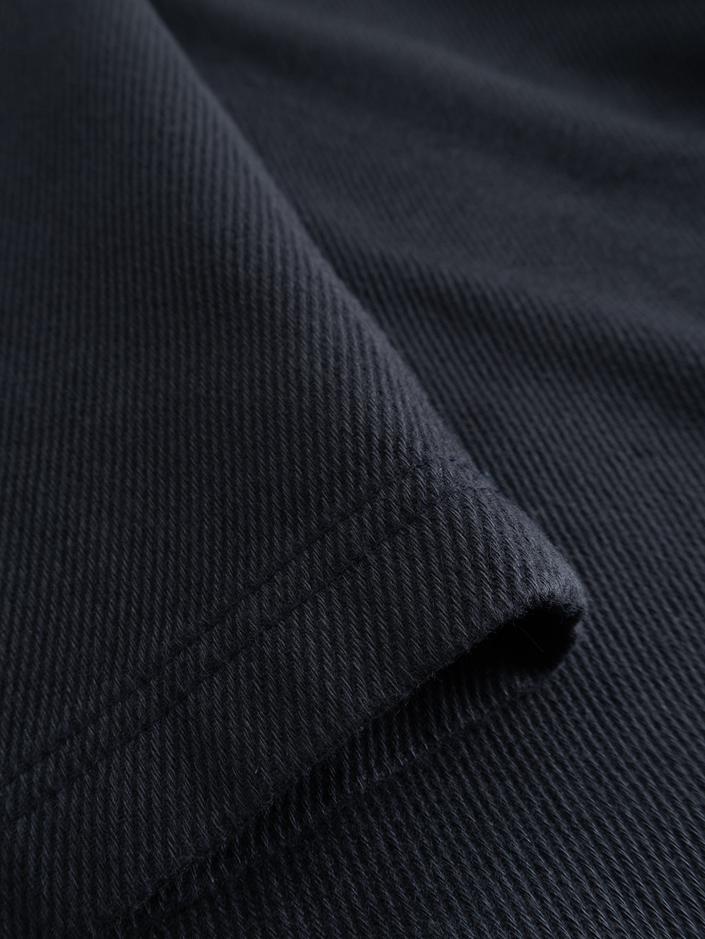 Close-up of a folded piece of GABJoe-Pas Vill - Blue Black ribbed cotton fabric from Gabba, highlighting its soft texture and subtle diagonal weave pattern—ideal for crafting relaxed fit or utility-inspired trousers in drapey cotton twill.