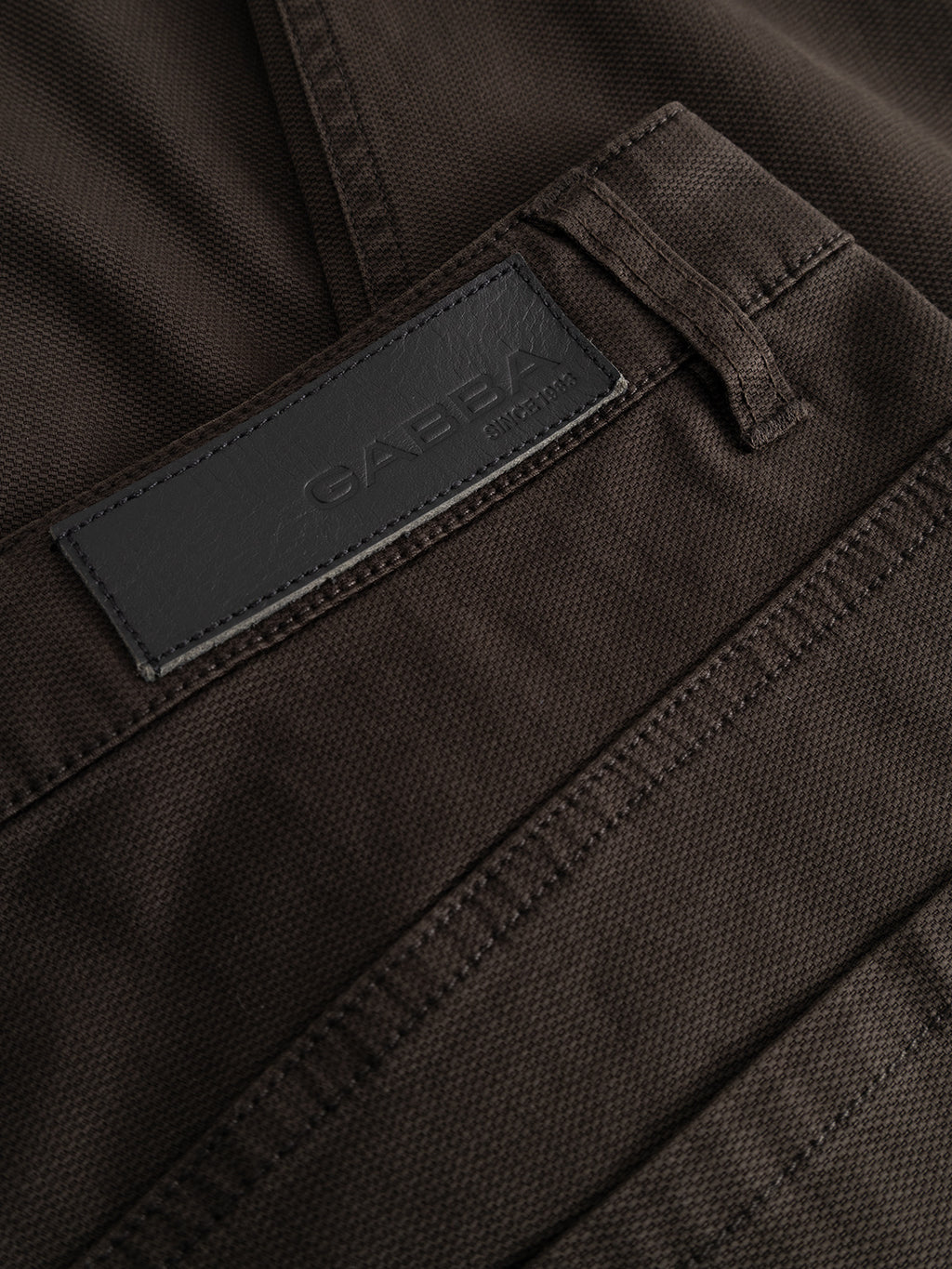 Close-up of dark brown “GABmarc 5poc Marlo - Brown Slate” pants with a black leather Gabba label stitched near the waistband. Designed for everyday wear, these regular fit jeans highlight the textured fabric and visible stitching details.