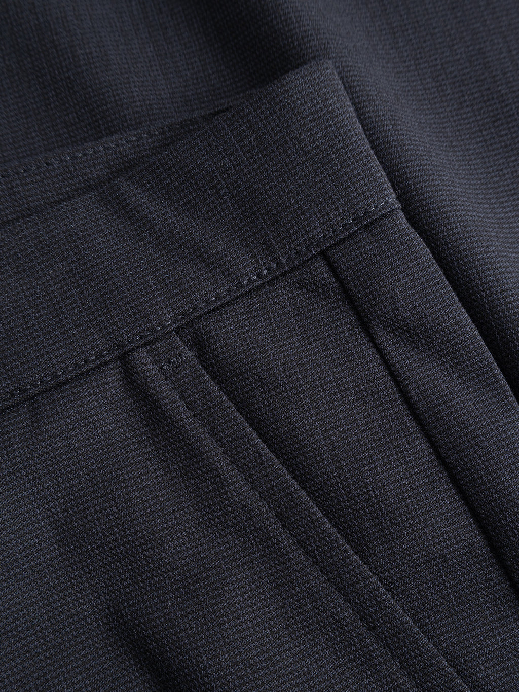 Close-up of the GABpaul Deme Pant in Dark Navy by Gabba, featuring a dark-colored, micro-pattern woven fabric with visible stitching and a seam—perfect details from these tailored trousers designed for everyday wear.