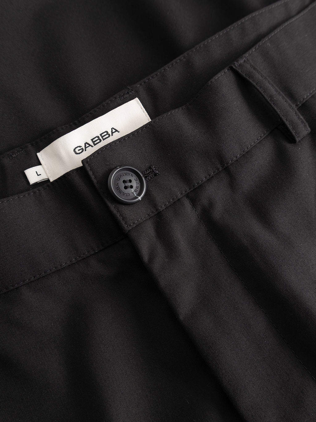 Close-up of the waistband on Gabba's GABjoe Turnup Fin Pant in black, featuring a black button and a white inner label reading GABBA L. The smooth, tailored fabric ensures a polished appearance.