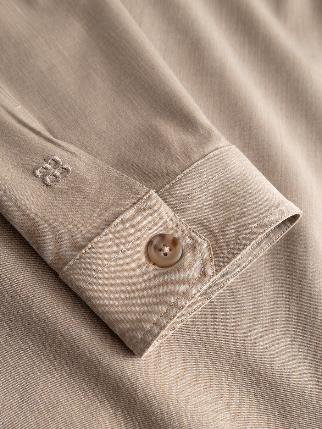 Close-up of the GABtogger Tailor Dressy Overshirt - Sand by Gabba, showcasing the beige wool-blend cuff with a single brown button and subtle “BB” embroidery above the cuff opening, highlighting the mélange fabric texture and precise stitching.