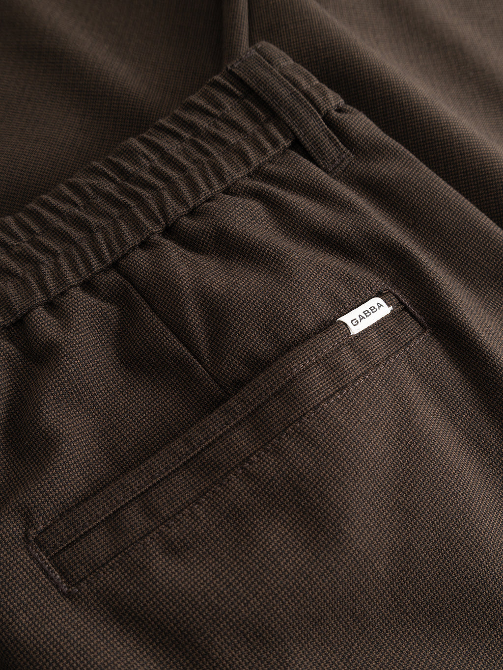 Close-up of the back pocket of the Gabba GABmonza Tasca Deme Pant in Brown Slate, featuring an elastic waistband and a small white Gabba label, crafted from micro-patterned fabric for enhanced texture and style.