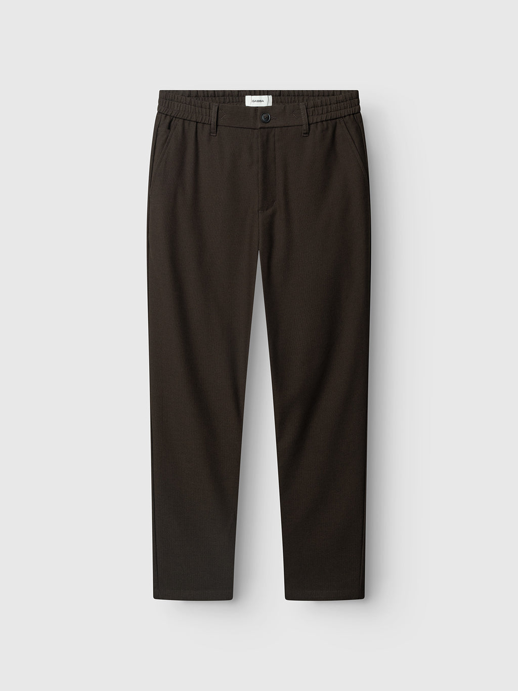 The GABmonza Tasca Deme Pant - Brown Slate by Gabba is a pair of dark brown, relaxed straight fit trousers featuring an elastic waistband, belt loops, side pockets, and a front button closure, crafted from micro-patterned fabric and displayed against a light gray background.