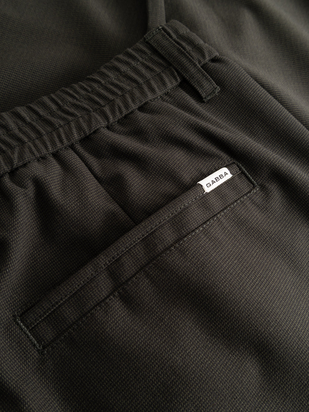 Close-up of the GABmonza Tasca Deme Pant by Gabba in Forest Night, featuring a cropped length, elastic waistband, and back pocket with a small white label reading “GABBA” sewn above it. The relaxed straight fit is crafted from micro-patterned fabric for subtle texture.