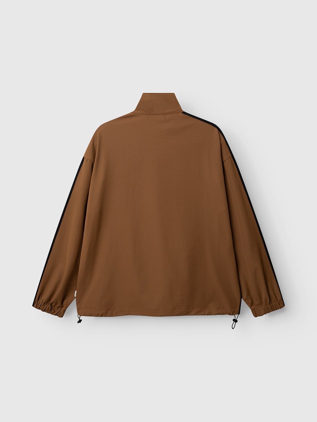 The GABtrack Nord Jacket - Brown by Gabba is shown from the back, highlighting its high collar, black stripes running down the sleeves, elastic cuffs, and adjustable drawstrings at the hem. This sporty fabric jacket stands out as a versatile casual layering piece with its boxy, tracksuit-inspired silhouette.