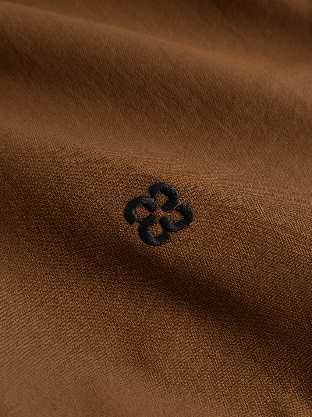 A close-up of the Gabba GABtrack Nord Jacket in brown showcases its sporty fabric with a clearly visible surface texture, featuring a small, black, embroidered geometric design at the center.