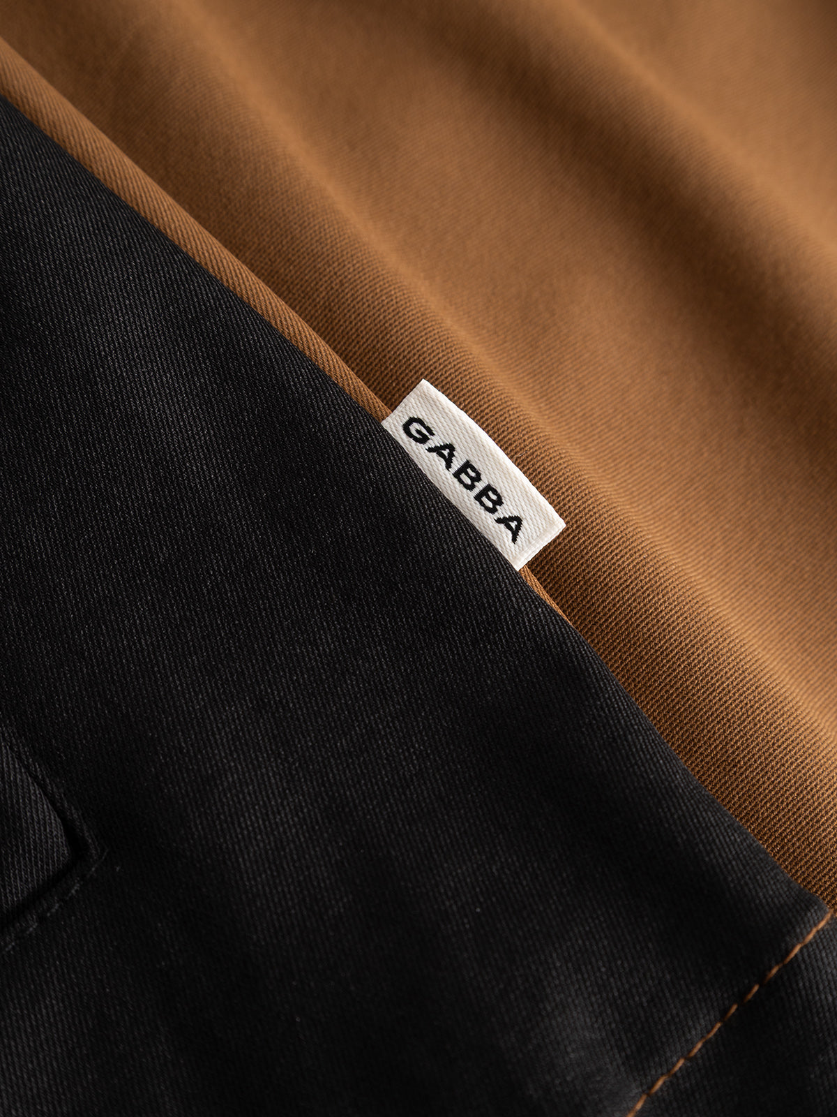 Close-up of a fabric label reading Gabba sewn onto the GABtrack Nord Jacket – Brown, with sporty black fabric and a hint of brown material visible in the background—an ideal casual layering piece for the modern wardrobe.