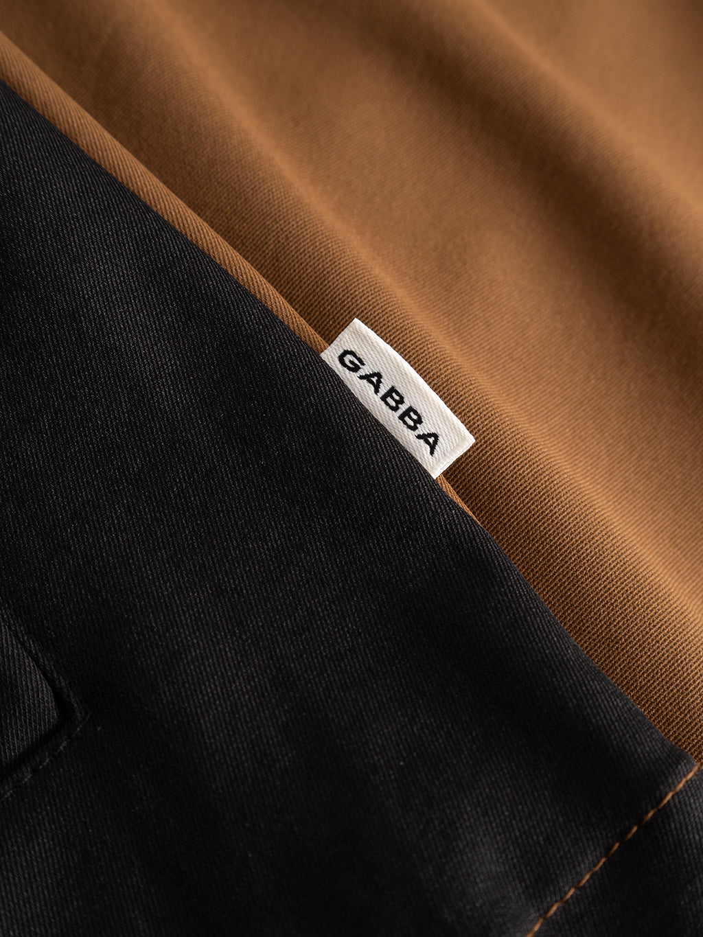 Close-up of a fabric label reading Gabba sewn onto the GABtrack Nord Jacket – Brown, with sporty black fabric and a hint of brown material visible in the background—an ideal casual layering piece for the modern wardrobe.