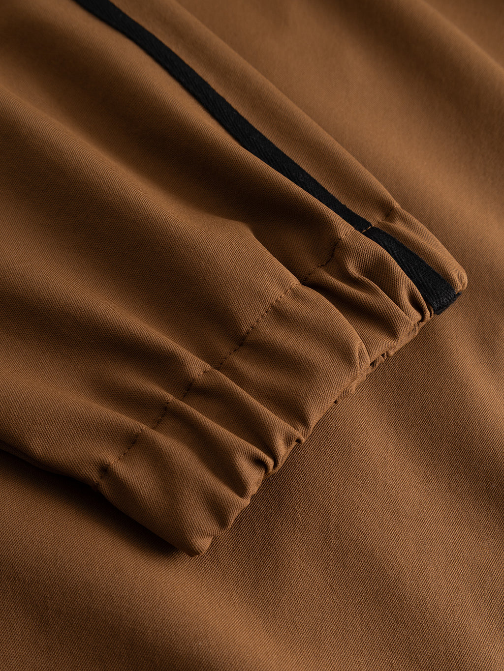 Close-up of the GABtrack Nord Jacket - Brown by Gabba, showcasing its sleeve with an elastic cuff and a black stripe running along its length, crafted from sporty fabric and laid flat on a matching brown background.