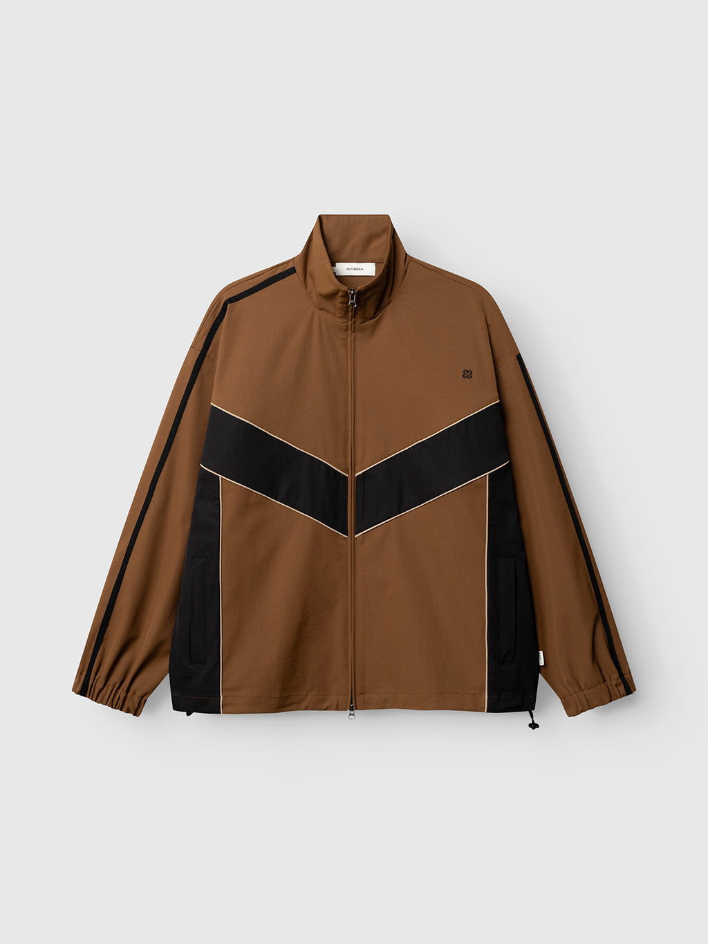 The Gabba GABtrack Nord Jacket in brown features a zip-up design with black diagonal stripes, white piping, and distinctive black side panels. Designed with a high collar and elastic cuffs, this sporty track jacket is ideal for casual layering and is showcased here against a plain light background.