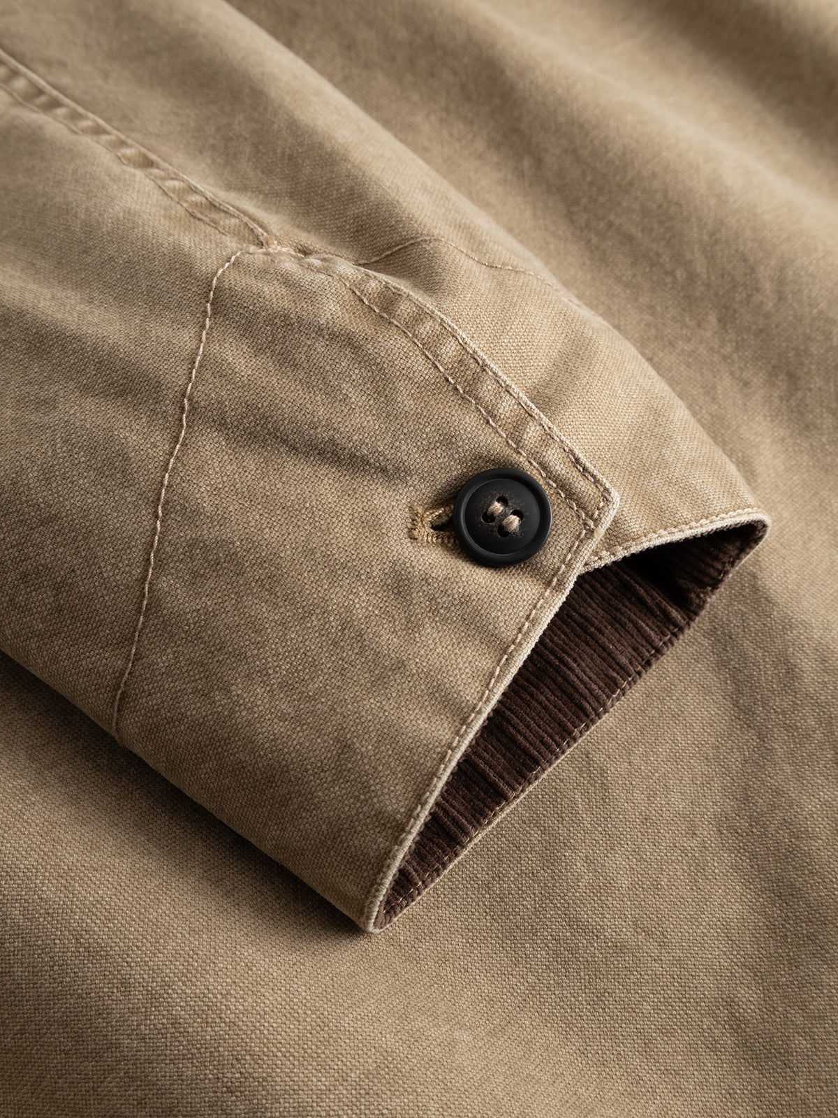 A close-up of the sleeve of the Gabba GABotto Tela Outerwear - Sand Crocker jacket highlights the visible stitching, black button, and brown lining inside the cuff.