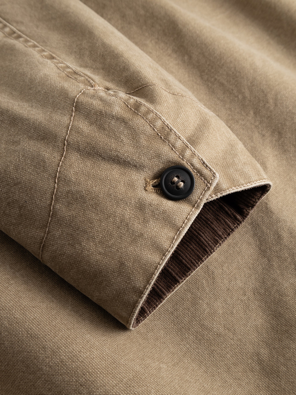 A close-up of the sleeve of the Gabba GABotto Tela Outerwear - Sand Crocker jacket highlights the visible stitching, black button, and brown lining inside the cuff.