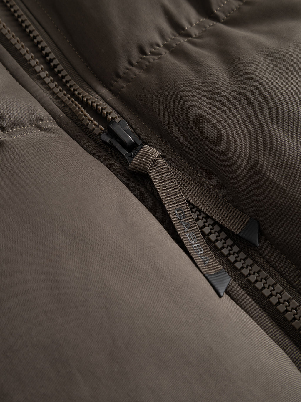 Close-up of a brown GABjulien Calle Outerwear - Brown Slate padded insulation jacket, featuring a matching zipper pull with an embossed logo.
