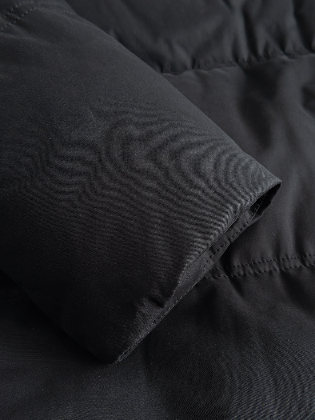 Close-up of a black padded GABjulien Calle Outerwear - Black jacket sleeve with a plain cuff.