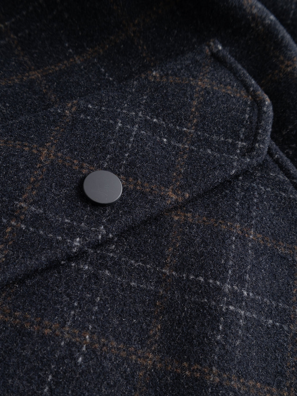 Close-up of the Gabba GABmatheo Check Bomber Jacket in Blue Check—a men’s outerwear piece crafted from a dark wool-blend with a checked pattern, flap pocket, and round metal button. The clear image highlights the fabric texture and precise stitching details.
