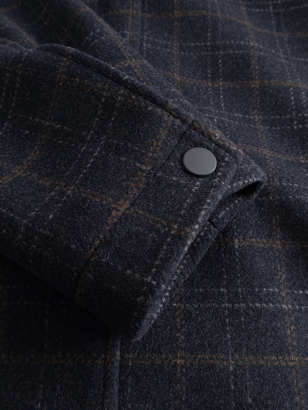 Close-up of the GABmatheo Check Bomber Jacket - Blue Check by Gabba shows its dark plaid wool-blend sleeve, detailed with a matte black snap button and understated brown lines in the checked pattern—an elevated choice in men’s outerwear.