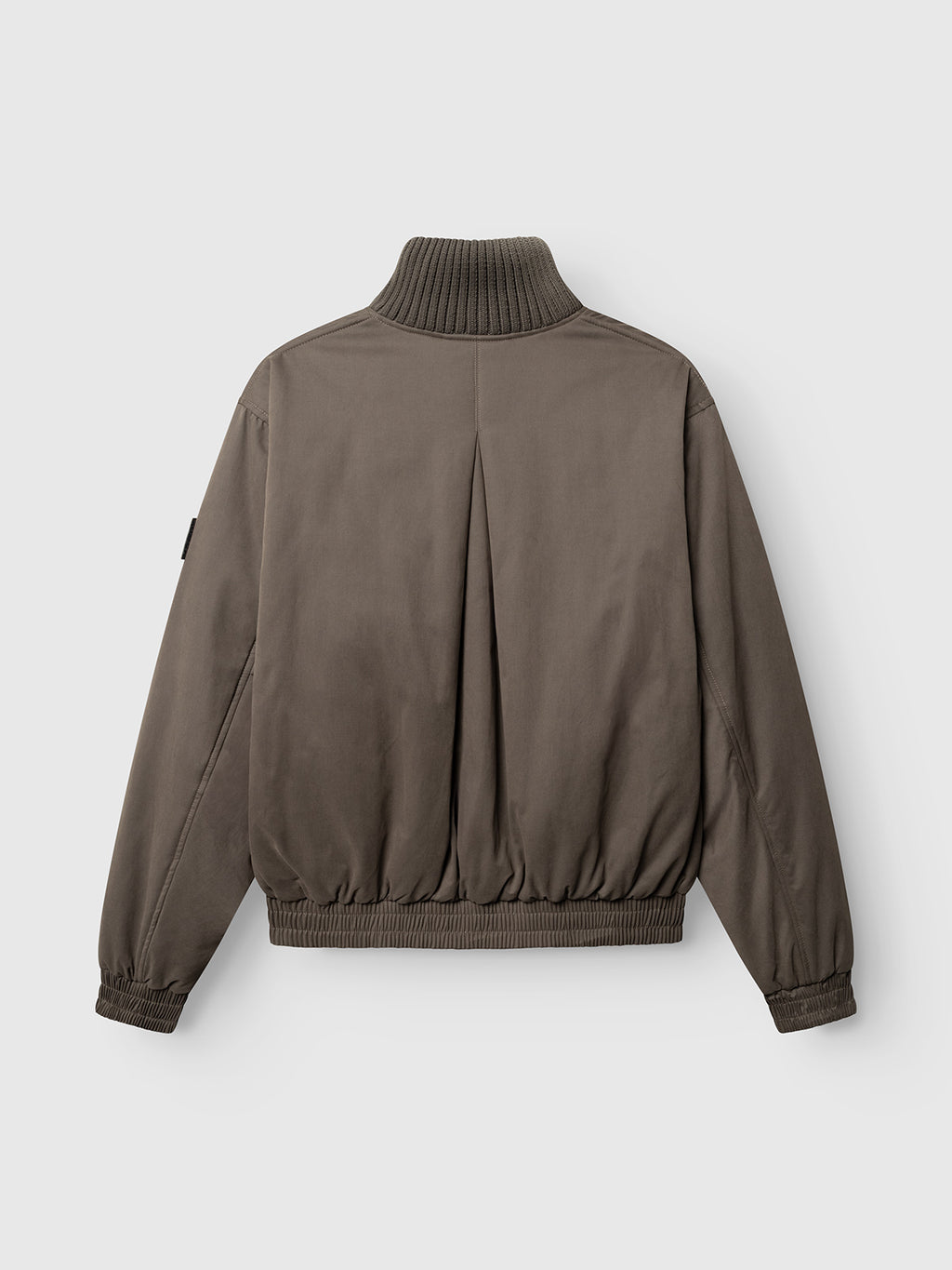 The GAByuri Calle Outerwear - Brown Slate by Gabba is a taupe bomber jacket shown from the back, featuring a ribbed high collar, ribbed cuffs and hem, a single back pleat, and loose-fitting sleeves. Lightly padded for comfort, this jacket offers a boxy relaxed fit, making it an essential piece of modern outerwear.