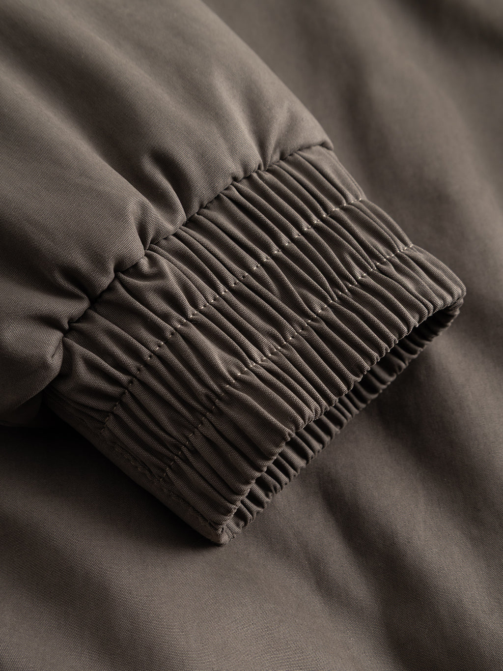 Close-up of the GAByuri Calle Outerwear - Brown Slate by Gabba, highlighting the brown lightly padded sleeve with an elastic, ribbed cuff. The smooth, slightly matte fabric and visible stitching at the cuff showcase a detail that enhances this modern piece from Gabba.
