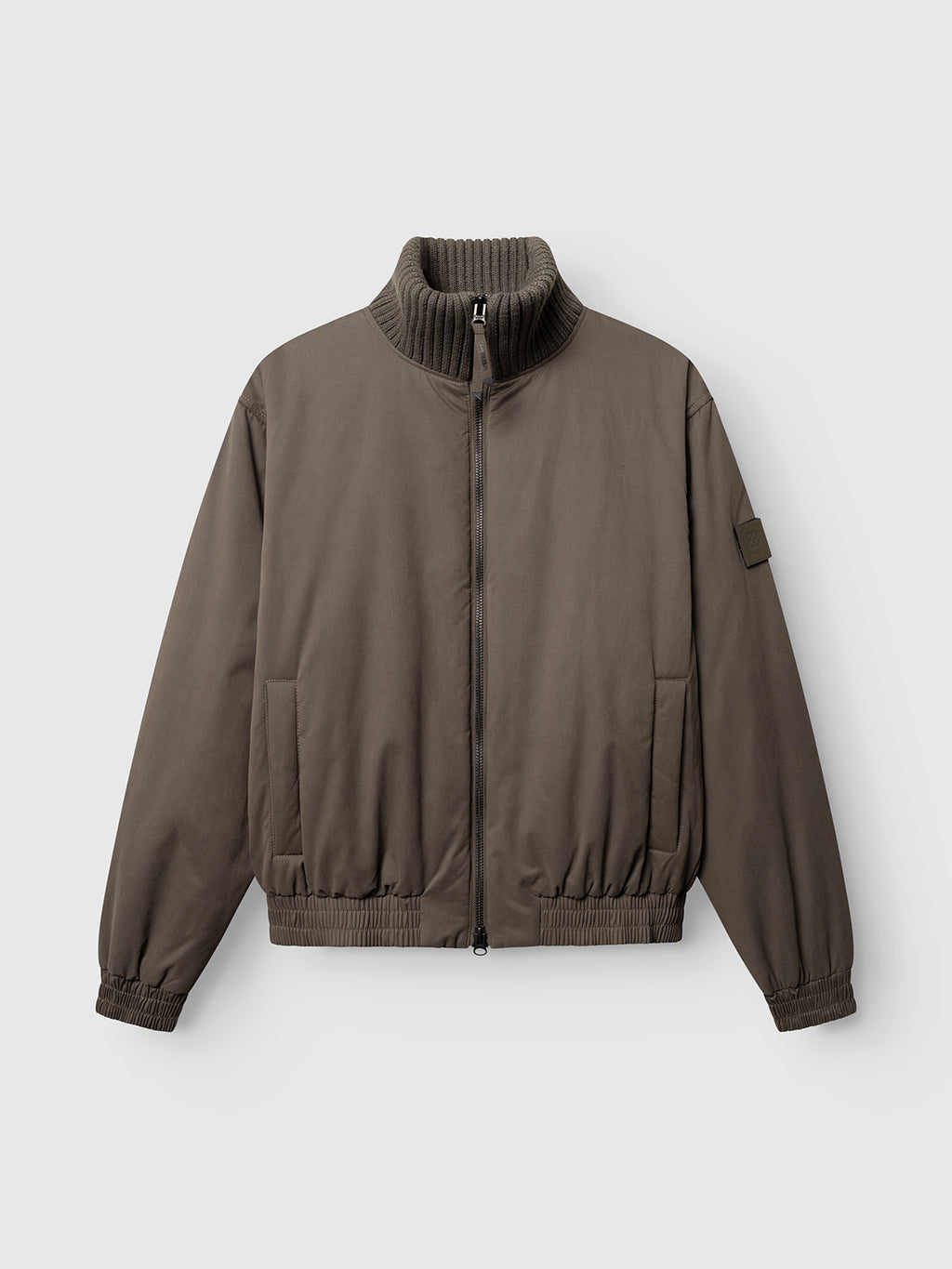 The GAByuri Calle Outerwear - Brown Slate by Gabba is a khaki-colored bomber jacket with a ribbed high collar, zip front, side pockets, and elastic cuffs and hem. Featuring a boxy relaxed fit for a contemporary outerwear look, it is lightly padded for added comfort and shown against a plain light gray background.