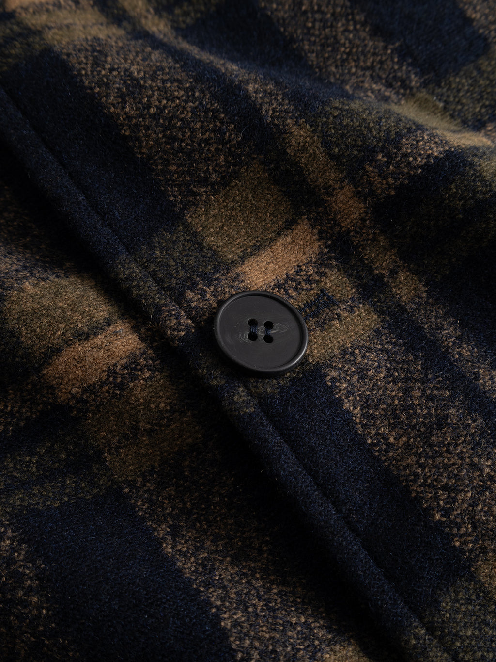 Close-up of the Gabba GABleeds Chezy Coat in Forest Night, a wool-blend checked outerwear essential featuring navy, beige, and brown plaid tones and a black four-hole button—expertly tailored for a sharp silhouette.