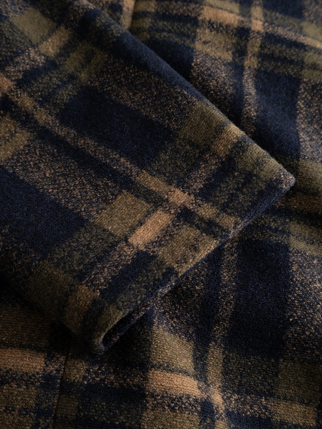 Close-up of dark blue and brown plaid fabric with a folded edge, highlighting the texture and intersecting lines of the pattern—an ideal match for the Gabba GABleeds Chezy Coat in Forest Night, a wool-blend checked coat that’s both an outerwear essential and effortlessly stylish.