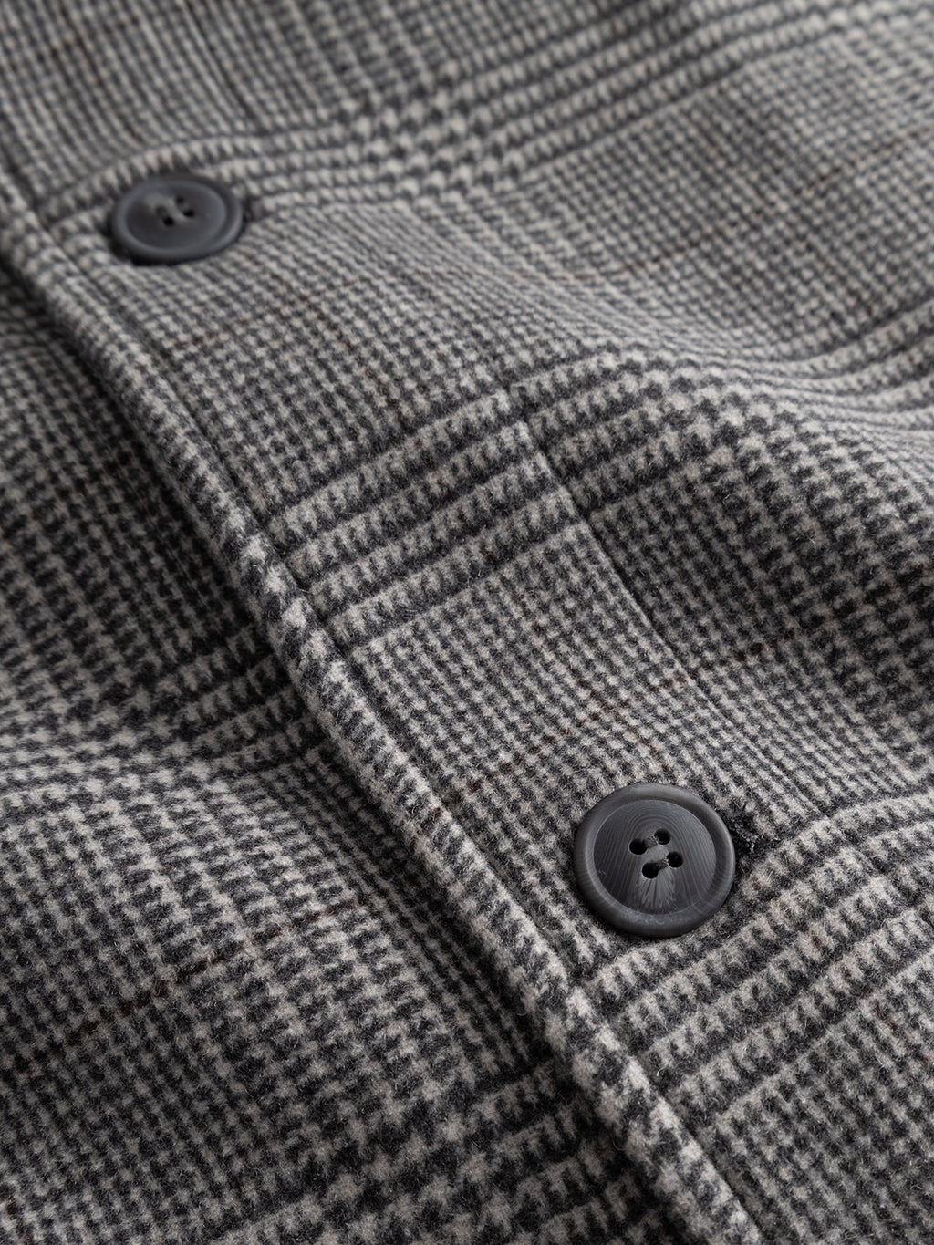 Close-up of the Gabba GABowen Scacco Coat in Grey Check, showcasing its gray and black wool-blend houndstooth pattern with two black buttons. The detailed texture and signature checked design of this tailored outerwear are clearly visible.