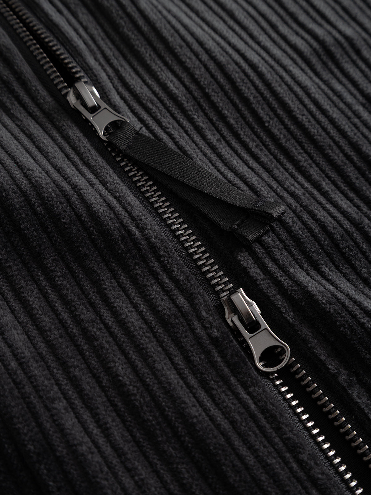 Close-up of the sturdy black zipper featured on the Gabba GABnik Zip Riglia GOTS Jacket in Dark Grey, partially unzipped to highlight the intricate metal teeth and pull tab set against the textured wide-wale corduroy—a distinctive detail that defines modern outerwear craftsmanship.