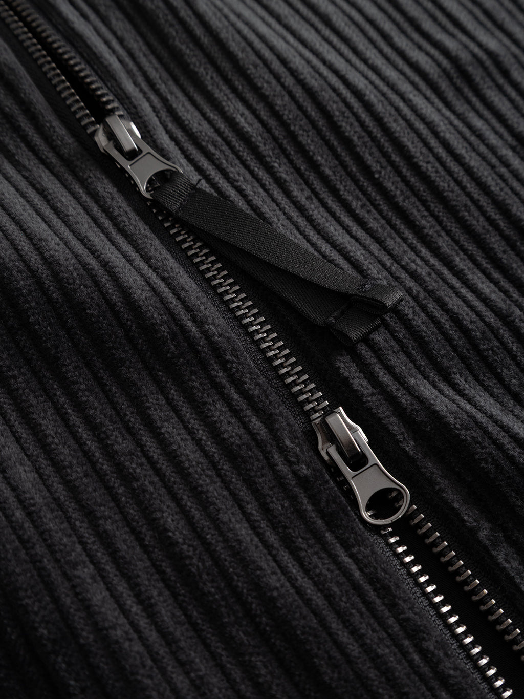 Close-up of the sturdy black zipper featured on the Gabba GABnik Zip Riglia GOTS Jacket in Dark Grey, partially unzipped to highlight the intricate metal teeth and pull tab set against the textured wide-wale corduroy—a distinctive detail that defines modern outerwear craftsmanship.