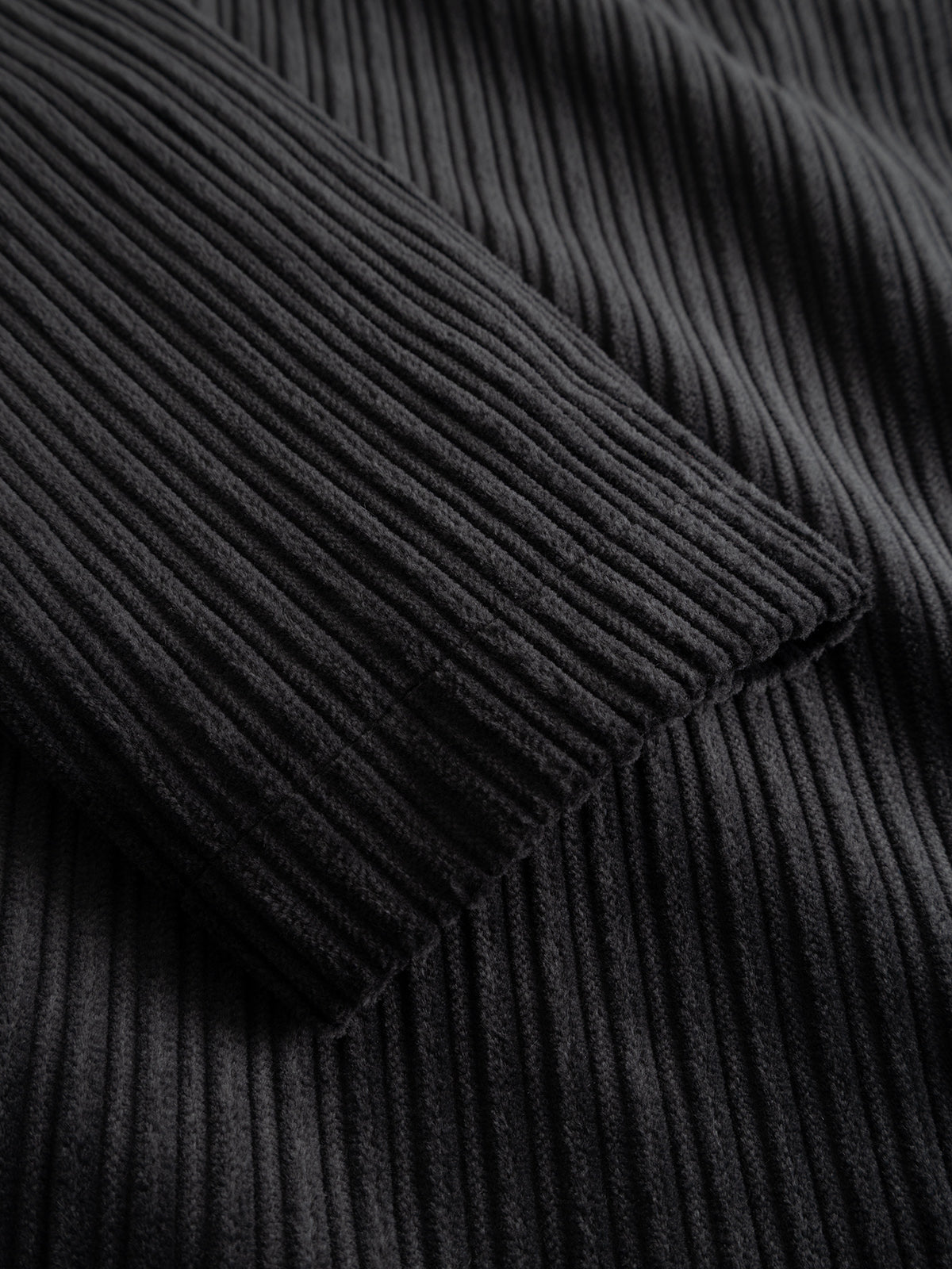 Close-up of the Gabba GABnik Zip Riglia GOTS Jacket in Dark Grey, highlighting the black ribbed fabric with detailed vertical textured lines reminiscent of wide-wale corduroy, and featuring a folded sleeve resting on top of the material.