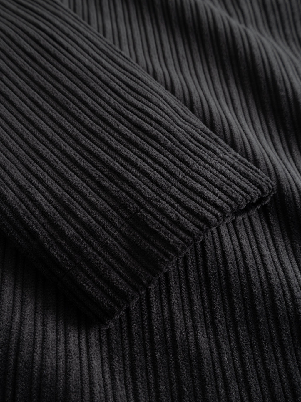 Close-up of the Gabba GABnik Zip Riglia GOTS Jacket in Dark Grey, highlighting the black ribbed fabric with detailed vertical textured lines reminiscent of wide-wale corduroy, and featuring a folded sleeve resting on top of the material.