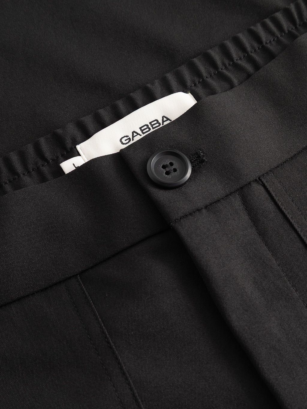 Close-up of the GABzeta Nord Work Pant in Meteorite by Gabba—a pair of black pants featuring a visible button and a partially exposed white Gabba label at the waistband, crafted from lightweight technical twill for a comfortable, workwear-inspired aesthetic.