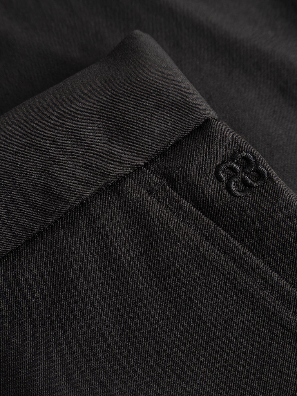 Close-up of the Gabba GABzeta Nord Work Pant in Meteorite, featuring black lightweight technical twill fabric with a visible pocket seam and an embroidered logo near the pocket opening. The image highlights the texture, precise stitching details, relaxed fit, and subtle workwear-inspired design elements.