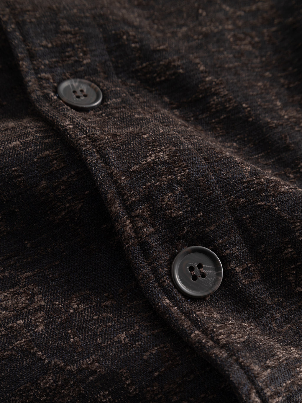 Close-up of the textured dark brown and black lyocell-blend jacquard fabric of the Gabba GABsimone Pockt Monte LS Overshirt in Brown Slate, featuring two black buttons sewn onto it. The fabric has a slightly mottled appearance, characteristic of this contemporary statement piece.