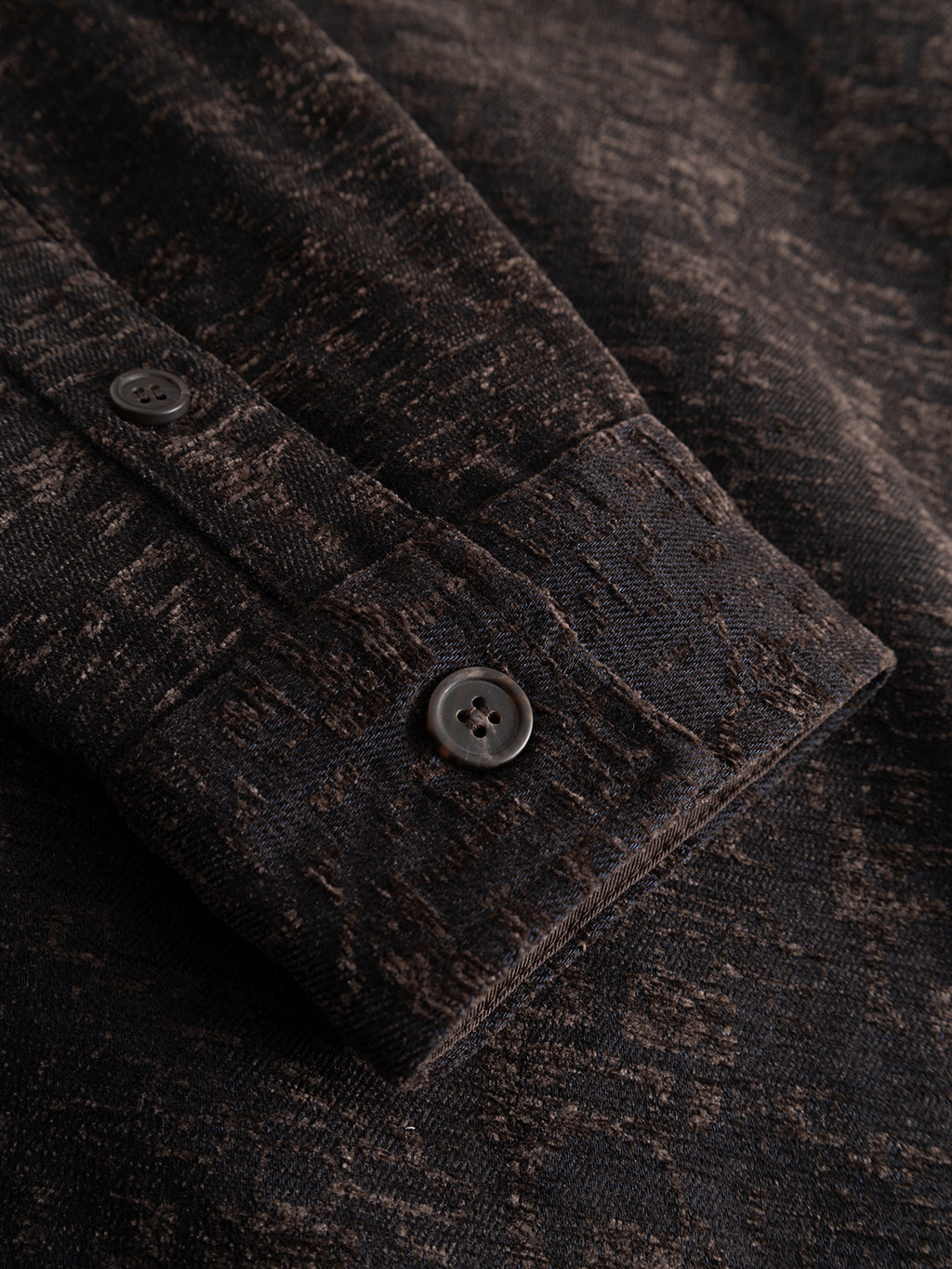 Close-up of the Gabba GABsimone Pockt Monte LS Overshirt in Brown Slate, featuring a dark brown, textured relaxed fit sleeve with a visible cuff and two round black buttons. The lyocell-blend jacquard fabric displays a subtle mottled pattern, lending it a slightly worn and rustic look.