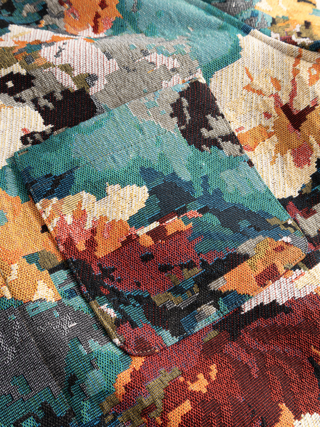 A close-up of the Gabba GABsimone Reso Fiore LS Overshirt - Multi Pattern shows its abstract, multicolored viscose-blend jacquard fabric in teal, ochre, orange, red, and black tones. This relaxed fit floral overshirt features a rectangular pocket that seamlessly integrates with the overall design.