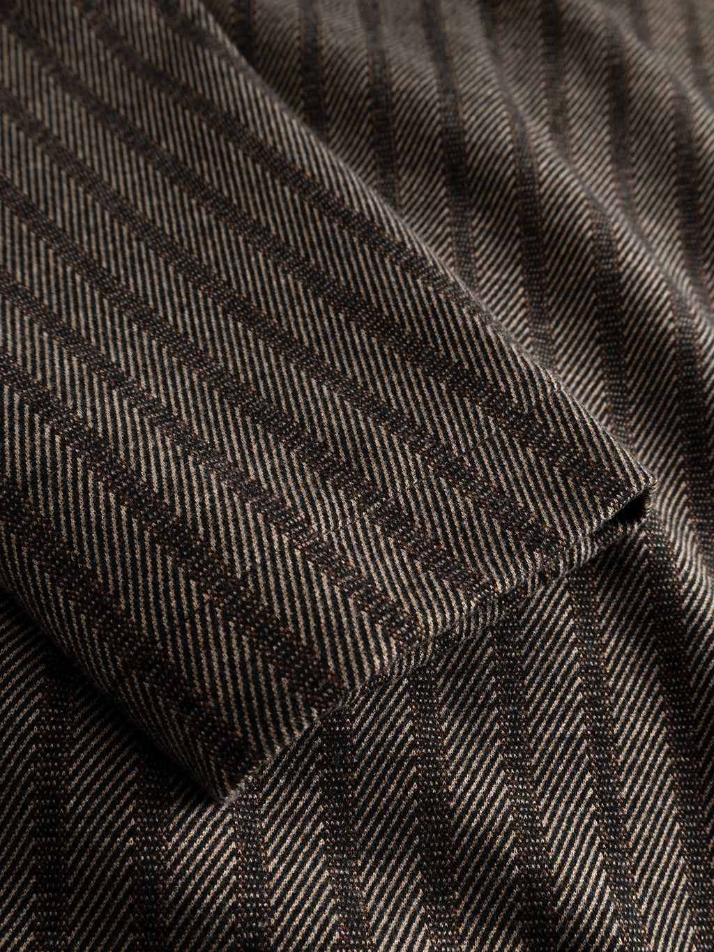 A close-up of the Gabba GABlibre AX Zapies LS Overshirt in Brown Slate highlights its regular fit fabric, featuring a diagonal herringbone pattern with dark vertical stripes and part of a folded sleeve or lapel—perfect for lightweight layering as an overshirt.
